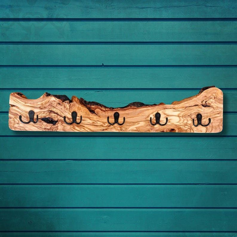 Handgemachte Garderobe aus Olivenholz mit natürlicher Baumkante und Metallhaken an der Wand.