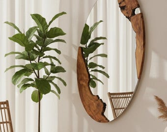 May include: Oval mirror with a wooden frame featuring a natural, irregular edge. The frame highlights the wood's grain and texture. The mirror is mounted on a neutral wall, reflecting a room with a plant and a chair. The mirror's dimensions are approximately 100 cm in height.