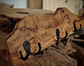 May include: A rustic wooden wall hook with a natural wood grain finish and three black metal hooks. The hook is made from a thick slab of wood with a live edge.