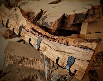 May include: A wooden coat rack with a natural wood finish and four black metal hooks. The rack is made from a single piece of wood with a unique grain pattern.