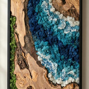 Puede incluir: Obra de arte enmarcada con un diseño natural. Combina madera, musgo y elementos texturizados. La paleta de colores incluye tonos de marrón, verde y azul, dentro de un marco negro. La obra evoca la naturaleza.
