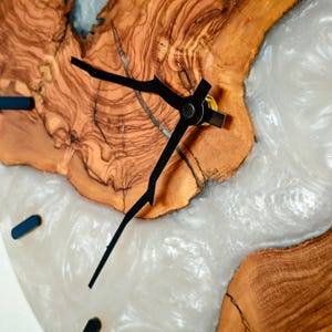 Może przedstawiać: Zbliżenie na tarczę zegara z czarnymi wskazówkami na drewnianej podstawie z białą żywicą. Drewno ma naturalny rysunek słojów.