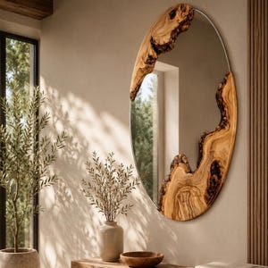 Peut inclure: Un miroir mural de forme ovale doté d'un cadre en bois naturel à bord brut. Le cadre présente un grain de bois brun clair avec des sections d'écorce sombres et texturées sur le haut et le côté droit, contrastant avec la surface en verre lisse.