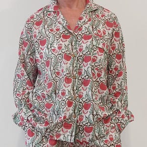 Peut inclure: Un ensemble de pyjama blanc à imprimé floral avec des fleurs rouges et des feuilles vertes. L'ensemble comprend une chemise à manches longues avec un devant boutonné et un pantalon assorti.