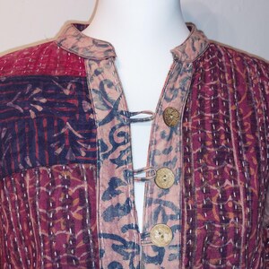 Peut inclure: Veste patchwork aux tons bordeaux, marine et beige. La veste présente un col officier, des boutons en bois et des coutures complexes. Le tissu présente un motif avec des éléments floraux et géométriques, créant une esthétique bohème.