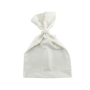 May include: A white, knotted fabric bag. The bag is made of a soft, opaque material. The top of the bag is tied in a knot, creating a handle. The bag is a solid, neutral color.