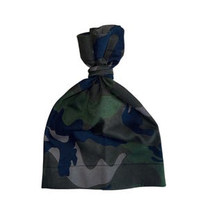 May include: A camouflage-patterned beanie hat in shades of green, blue, and gray. The hat is made of soft fabric and features a knotted top. The design is a classic military-inspired print, suitable for various styles.