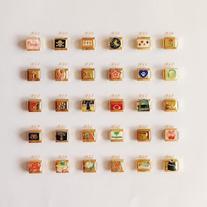 Puede incluir: Una colecci&oacute;n de treinta eslabones modulares dorados para pulsera, dispuestos en cinco filas de seis. Cada eslab&oacute;n cuadrado presenta un dise&ntilde;o &uacute;nico en esmalte de colores, incluyendo s&iacute;mbolos como una calavera, coraz&oacute;n, estrella, gato, cereza.