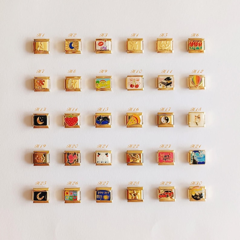 Puede incluir: Una colecci&oacute;n de treinta eslabones modulares dorados para pulsera tipo charm, dispuestos en una cuadr&iacute;cula. Cada eslab&oacute;n cuadrado presenta un dise&ntilde;o &uacute;nico en esmalte de colores, incluyendo s&iacute;mbolos como fresa, cereza, gato, luna, sol y varios patrones.
