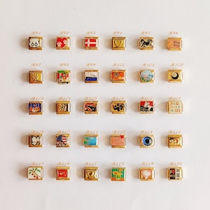 Puede incluir: Una colecci&oacute;n de treinta eslabones modulares dorados para pulsera dispuestos en cinco filas. Cada eslab&oacute;n cuadrado presenta un dise&ntilde;o de esmalte &uacute;nico, incluyendo s&iacute;mbolos como una se&ntilde;al de la Ruta 66, corazones, banderas, animales y texto.
