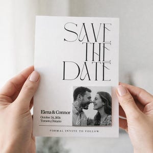 May include: A white rectangular save the date card featuring black serif typography. The text reads Save The Date, Elena & Connor, October 24, 2026, Toronto, Ontario, and Formal Invite To Follow. A black and white photo of a couple is attached.