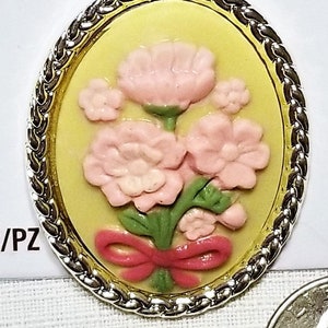 May include: A silver-toned pendant with a yellow oval cameo featuring a pink flower bouquet with a red bow. The pendant is 1.85 inches (4.7 cm) tall and 1.46 inches (3.7 cm) wide. The packaging includes the text "MARTHA STEWART CRAFTS" and "pendant, pendentif, pendiente".