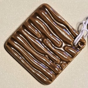 May include: A brown ceramic tile with a wood grain pattern. The tile is square and has a glossy finish.