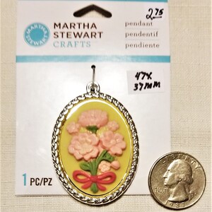 May include: A silver pendant with a yellow and pink floral design. The pendant is 1.85 inches in diameter and is labeled "Martha Stewart Crafts".