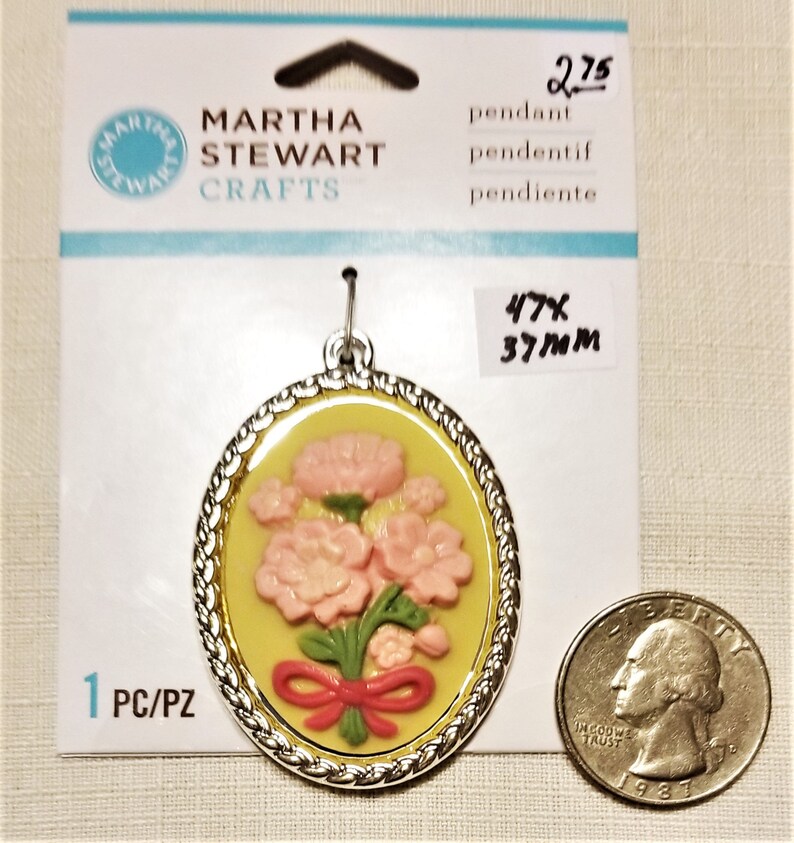 May include: A silver pendant with a yellow and pink floral design. The pendant is 1.85 inches in diameter and is labeled "Martha Stewart Crafts".