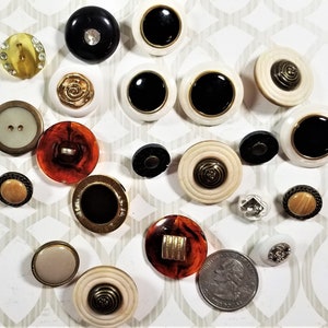 May include: Assortment of vintage buttons in various colors, patterns, and materials, including white, black, brown, gold, and ivory. Some buttons have a raised design, while others are flat. The buttons are arranged on a white surface with a patterned background.