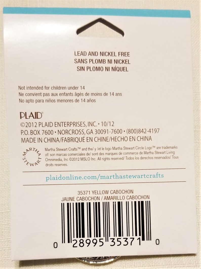 May include: A close-up of a product label for 35371 Yellow Cabochon. The label is white with black text and a barcode. The text on the label reads "Lead and Nickel Free", "Sans Plomb Ni Nickel", "Sin Plomo Ni Niquel", "Not intended for children under 14", "Ne convient pas aux enfants ages de moins de 14 ans", "No apto para ninos menores de 14 anos", "PLAID", "&copy;2012 PLAID ENTERPRISES, INC. 10/12", "P.O. BOX 7600 NORCROSS, GA 30091-7600 (800)842-4197", "MADE IN CHINA/FABRIQU&Eacute; EN CHINE/HECHO EN CHINA", "Martha Stewart Crafts&trade; and the/ y /et le logo Martha Stewart Circle Logo&trade; are trademarks of/ son marcas comerciales de/ sont des marques de commerce de Martha Stewart Living Omnimedia, Inc. &copy;2012 MSLO Inc. All rights reserved/ Todos los derechos reservados/Tous droits reserves.", "plaidonline.com/marthastewartcrafts", "35371 YELLOW CABOCHON", "JAUNE CABOCHON/AMARILLO CABOCHON".