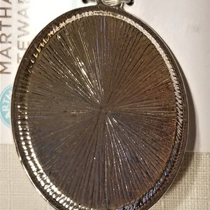 May include: Silver-toned round metal pendant with a textured surface. The pendant has a loop at the top for attaching to a chain or cord.