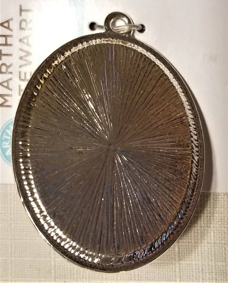 May include: Silver-toned round metal pendant with a textured surface. The pendant has a loop at the top for attaching to a chain or cord.