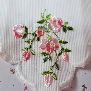 May include: A white cotton handkerchief with a delicate embroidered design of pink roses and green leaves.