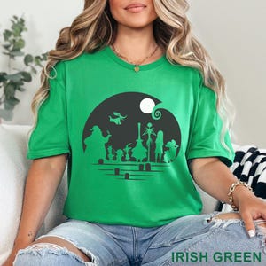 Pu&ograve; includere: Una maglietta verde con una grafica nera raffigurante personaggi di un film, ambientata su sfondo di luna crescente e luna piena. Il testo "IRISH GREEN" &egrave; in basso nell'immagine.