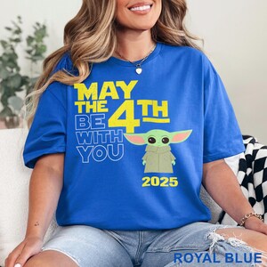 May include: A royal blue t-shirt with a yellow graphic that says "May the 4th Be With You" and features a cartoon image of Baby Yoda. The year 2025 is printed below the graphic.