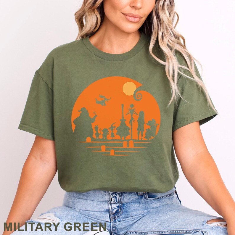 Pu&ograve; includere: T-shirt verde militare con grafica arancione di sagome di un film a tema Halloween. Il design include personaggi, una luna e una spirale. Il testo "MILITARY GREEN" &egrave; in basso.