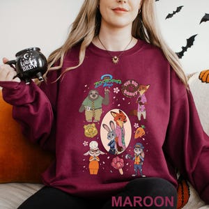 May include: Maroon sweatshirt featuring characters from the animated film Zootopia. The design includes Judy Hopps, Nick Wilde, and other characters. The text "Zootopia" and "The Big Donut" are also visible. The word "MAROON" is printed at the bottom.