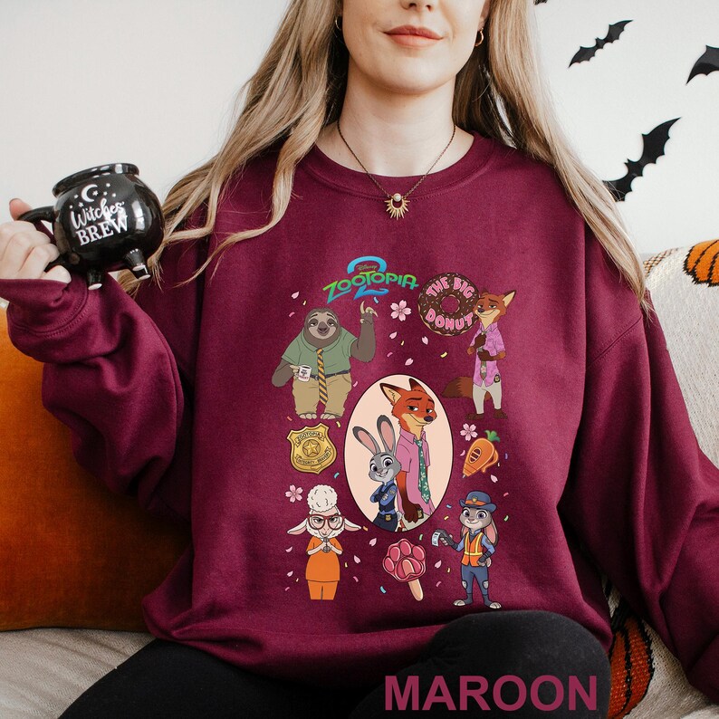 May include: Maroon sweatshirt featuring characters from the animated film Zootopia. The design includes Judy Hopps, Nick Wilde, and other characters. The text "Zootopia" and "The Big Donut" are also visible. The word "MAROON" is printed at the bottom.