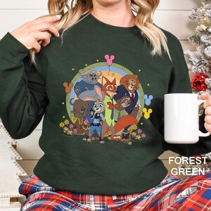 May include: Dark green sweatshirt with a cartoon illustration of animal characters, including a fox, lion, and bunny. The design is set against a rainbow and floral background. The text "FOREST GREEN" is at the bottom of the image.