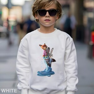 Peut inclure: Sweat-shirt blanc avec un motif color&eacute; de personnages du film d'animation Zootopie. Le motif comprend un renard en chemise rose, un lapin et un serpent bleu. Le mot "WHITE" est imprim&eacute; en bas.