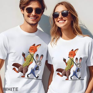 Pode incluir: T-shirts brancas com um desenho de raposa e coelho de desenho animado. A raposa usa uma camisa verde e cal&ccedil;as marrons, segurando um telefone. O coelho est&aacute; de uniforme azul. A palavra "WHITE" est&aacute; impressa na parte inferior.