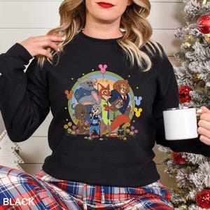 May include: Black crew neck sweatshirt with a colourful graphic of characters from the animated film Zootropolis. The design includes Judy Hopps, Nick Wilde, and other characters. The word "BLACK" is printed at the bottom.