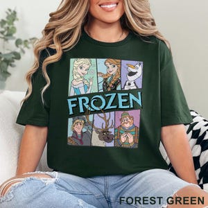 May include: Forest green t-shirt featuring a graphic of characters from the animated film "Frozen." The design includes Elsa, Anna, Olaf, Kristoff, Sven, and Oaken, with the word "FROZEN" in blue. The shirt is made of a soft material.