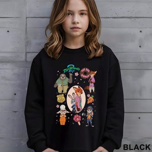 May include: Black sweatshirt featuring characters from the animated film Zootopia. The design includes Judy Hopps, Nick Wilde, and other characters, along with the text "Zootopia 2" and "The Big Donut". The word "BLACK" is printed at the bottom right.