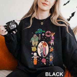 May include: Black crewneck sweatshirt featuring a colorful graphic of characters from the animated film Zootopia. The design includes Judy Hopps, Nick Wilde, and other characters, along with the text "Zootopia" and "The Big Donut". The word "BLACK" is printed at the bottom.