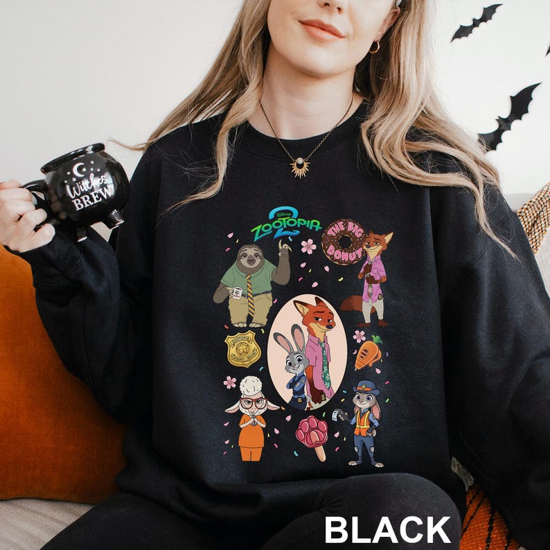 May include: Black crewneck sweatshirt featuring a colorful graphic of characters from the animated film Zootopia. The design includes Judy Hopps, Nick Wilde, and other characters, along with the text "Zootopia" and "The Big Donut". The word "BLACK" is printed at the bottom.