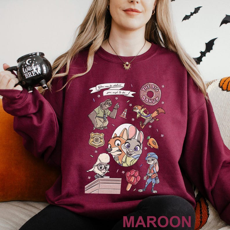 Może przedstawiać: Bordowa bluza z postaciami z kresk&oacute;wek i napisem "You can be whatever you wish to be." Projekt zawiera pączka i r&oacute;żne postacie zwierząt. Słowo "MAROON" jest wydrukowane na dole.