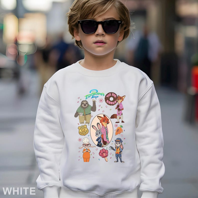 May include: White sweatshirt featuring characters from the animated movie "Zootopia". The design includes a sloth, fox, bunny, and other characters. The text "Zootopia 2" and "The Big Donut" are also visible. The sweatshirt is worn by a person wearing sunglasses.