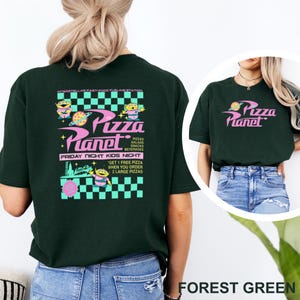 May include: Forest green t-shirt featuring the Pizza Planet logo in pink and yellow. The back of the shirt has a larger graphic with the text "Pizza Planet" and alien characters, with the words "Friday Night Kids Night".