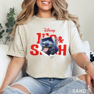 Puede incluir: Camiseta color arena con un gr&aacute;fico de Stitch de Lilo & Stitch de Disney. El texto rojo dice "Lilo & Stitch" con Stitch saliendo de un efecto de papel rasgado. El logotipo de Disney est&aacute; en la parte superior.