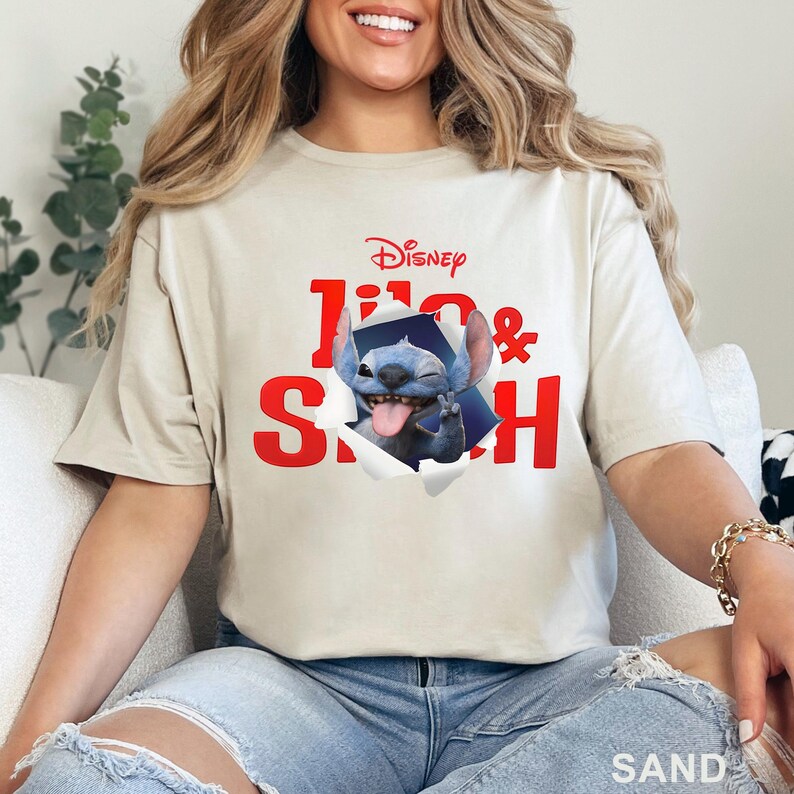 Puede incluir: Camiseta color arena con un gr&aacute;fico de Stitch de Lilo & Stitch de Disney. El texto rojo dice "Lilo & Stitch" con Stitch saliendo de un efecto de papel rasgado. El logotipo de Disney est&aacute; en la parte superior.