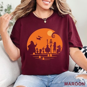 Pu&ograve; includere: T-shirt bordeaux con una silhouette di personaggi di un popolare film d'animazione su un cerchio arancione con una luna. Il testo "MAROON" &egrave; in basso. La maglietta &egrave; di colore bordeaux unito.