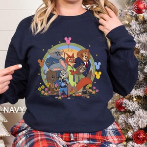 May include: Navy blue sweatshirt with a colourful graphic of animated movie characters. The design includes a rainbow, flowers, and the word "NAVY" on the bottom left. The sweatshirt has a crew neck and long sleeves.