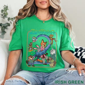 Pode incluir: Camiseta verde irland&ecirc;s com um gr&aacute;fico colorido do filme Zootopia. O design inclui a palavra "Zootopia" e v&aacute;rios personagens de desenhos animados. A camiseta &eacute; feita de um material macio.