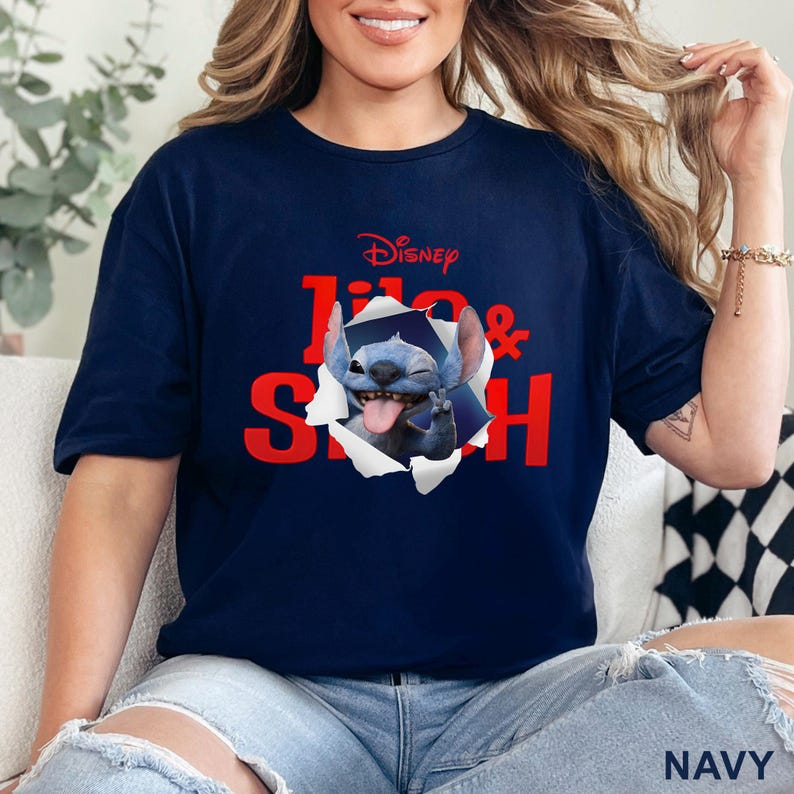 Puede incluir: Camiseta azul marino con el logo de Disney y las palabras "Lilo & Stitch" en rojo. El gr&aacute;fico muestra a Stitch saliendo de un agujero rasgado. La palabra "NAVY" est&aacute; impresa en la parte inferior.