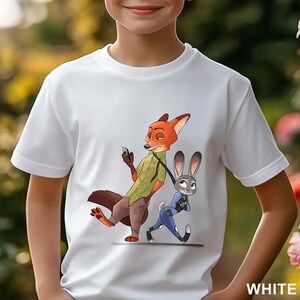 Pode incluir: Camiseta branca com uma ilustra&ccedil;&atilde;o de desenho animado de Nick Wilde e Judy Hopps de Zootopia. Nick, uma raposa laranja, est&aacute; segurando um telefone, enquanto Judy, uma coelha cinza, anda ao lado dele. A palavra "WHITE" est&aacute; impressa no canto inferior direito.