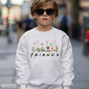May include: White sweatshirt featuring a colorful graphic of cartoon animals holding balloons above the word "FRIENDS" in black. The sweatshirt is a crew neck style.