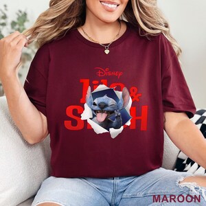 Puede incluir: Camiseta granate con los personajes de Disney Lilo & Stitch. El gr&aacute;fico muestra a Stitch saliendo de un agujero rasgado, gui&ntilde;ando un ojo y sacando la lengua. El texto "Lilo & Stitch" es rojo, con el logo de Disney encima.