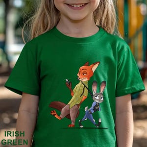 Pode incluir: Camiseta verde irland&ecirc;s infantil com uma ilustra&ccedil;&atilde;o de desenho animado de uma raposa e um coelho. A raposa est&aacute; vestindo uma camisa verde e segurando um telefone, enquanto o coelho est&aacute; com um uniforme azul. A frase "IRISH GREEN" est&aacute; impressa na parte inferior.